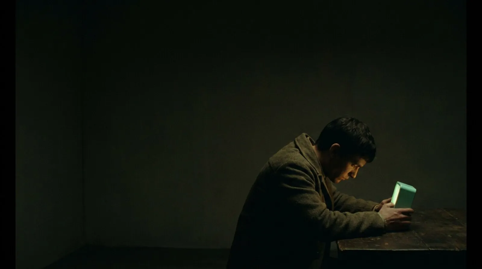 a figure at a dim desk polishing one small mint-green light in an otherwise dark room. the post's thesis in one frame: focused on the wrong moment.